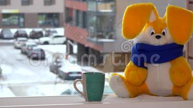冬天，黄色玩具兔子拿着茶杯坐在窗边。 雪花<strong>飘落</strong>。